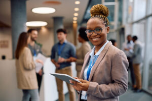 Happy African American public speaker with digital tablet during business conference looking at camera.